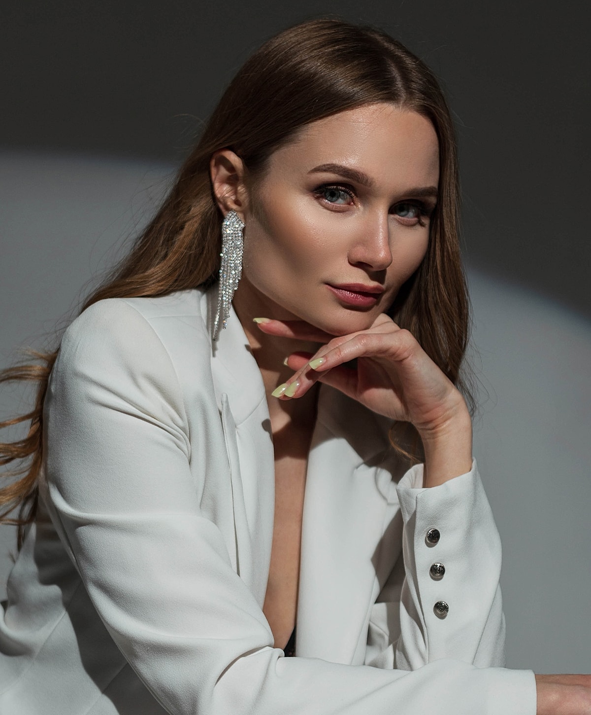 Woman in white blazer with elegant earrings.