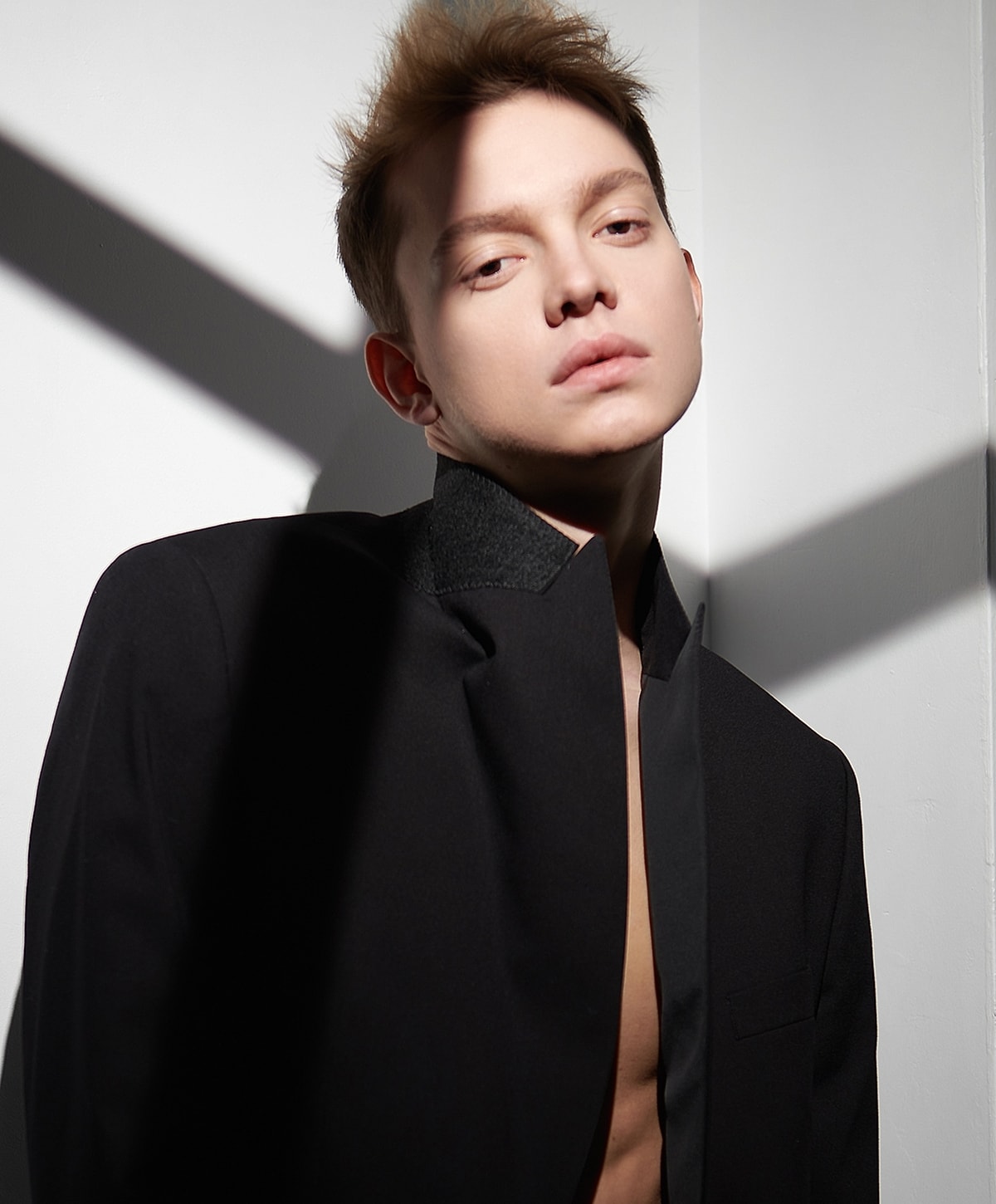 Model posing in stylish black jacket with shadows.